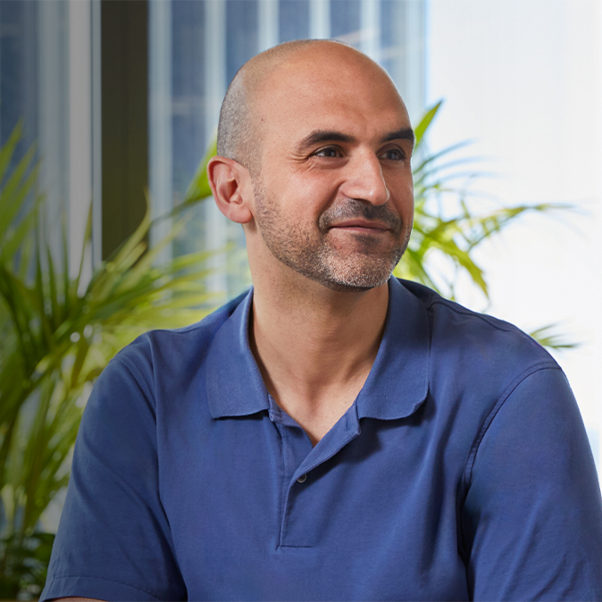 Ahmed sitter inomhus, ler och tittar åt vänster, bort från kameran.