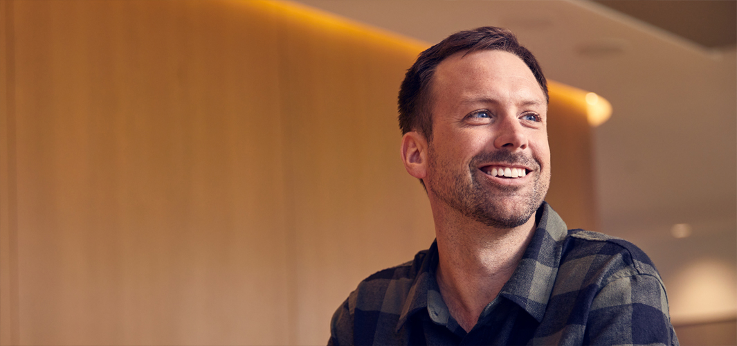 Jordan sitter smilende med hendene foldet på bordet foran seg.