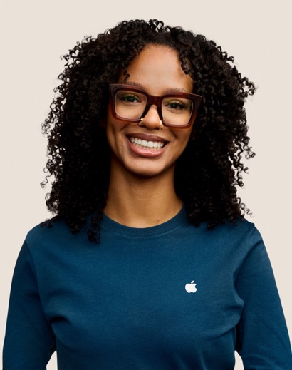 Portrait of a smiling Apple Retail team member with long, curly dark hair and glasses.