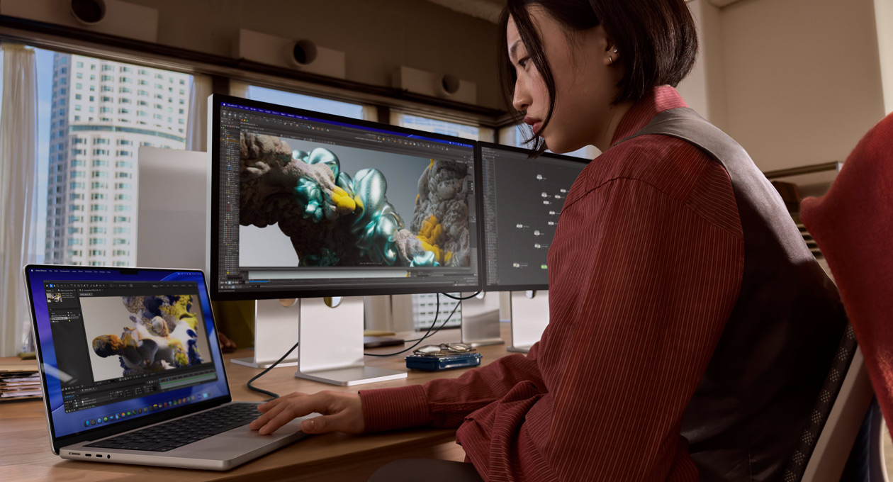 Una persona en una oficina trabaja en un portátil MacBook conectado a un Studio Display XDR mediante un puerto Thunderbolt 5