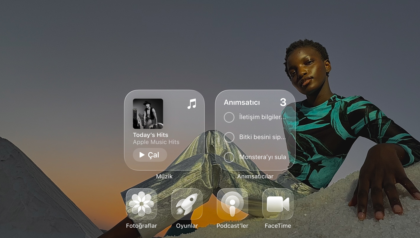 Liquid Glass ekrandaki Apple Music, Anımsatıcılar, Fotoğraflar, Oyunlar, Podcast’ler ve FaceTime gibi şeffaf uygulama simgeleri duvar kağıdını yansıtıyor