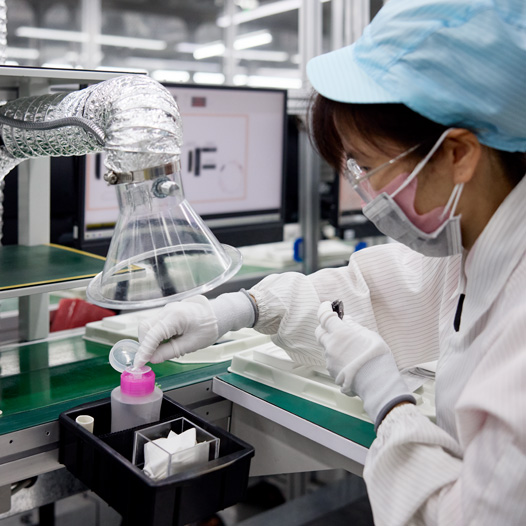 An employee in full safety uniform works at a station at an Apple Watch assembly facility