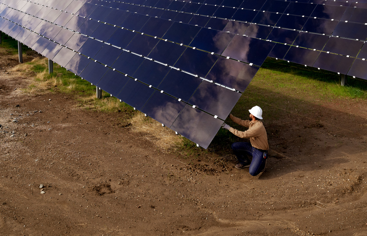 An employee in a safety hat inspects solar array that is in a field