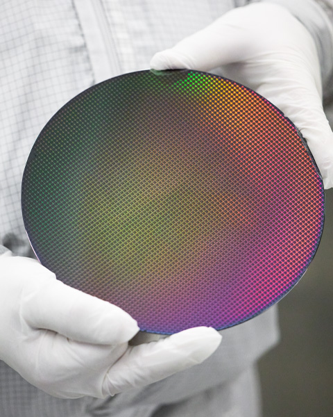 Two gloved hands hold a silicon wafer